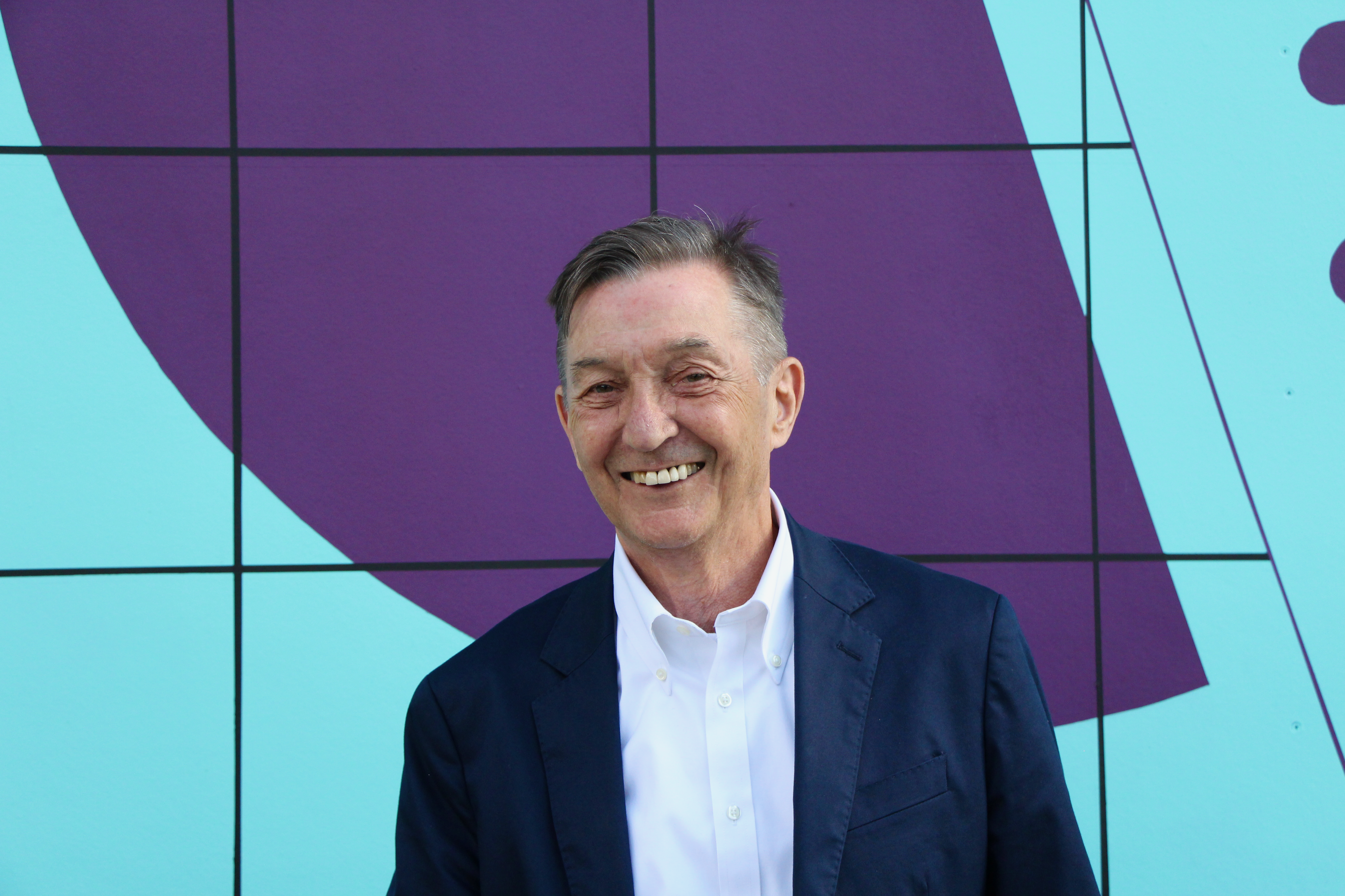 David LePage smiles at the camera in front of a painted purple and turquoise wall.